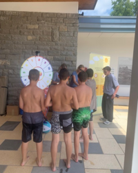 Auf dem Bild sind Jungs von hinten vor dem Glücksrad zu sehen.