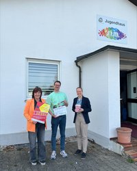 Auf dem Bild sieht man das Veranstaltungsteam, bestehend aus drei Personen, vor dem Jugendhaus JiM in Mindelheim. Die 3 Personen haben eine Popcorntüte, eine Filmklappe und das Plakat zur Filmreihe in der Hand. 