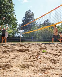 Sandplatz mit Netz, vier Sportlerinnen und Sportler spielen gerade.
